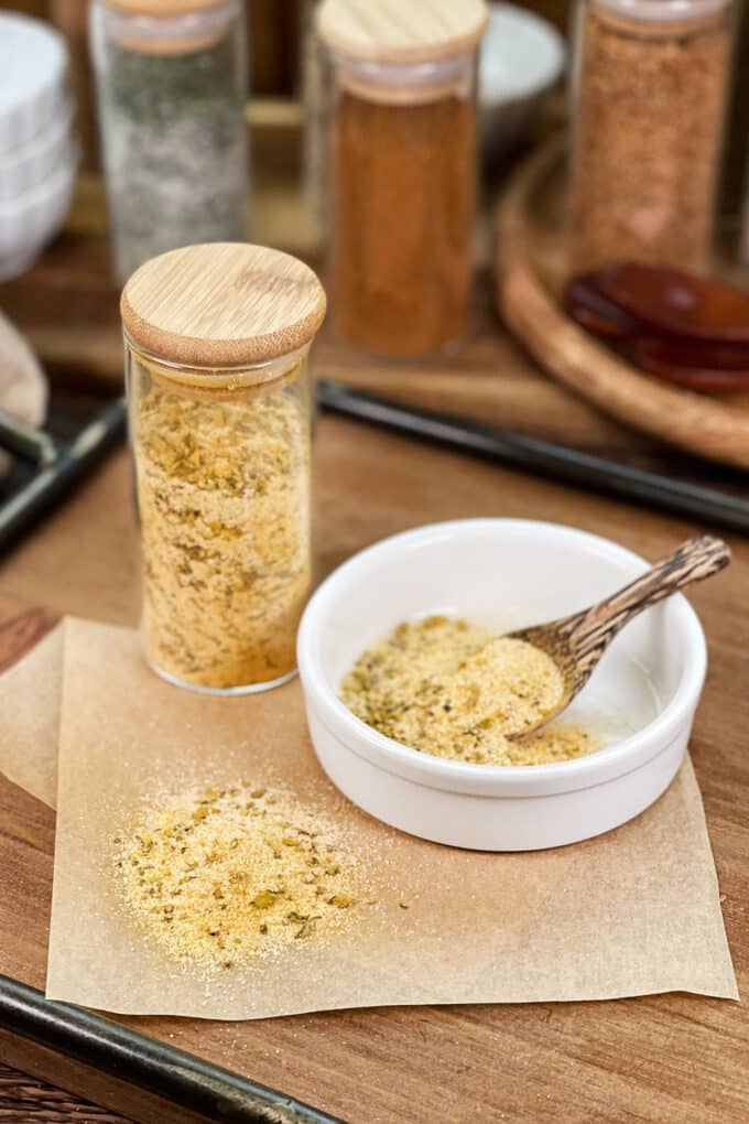 Homemade Adobo seasoning in glass jar, in dish with spoon, and spilled on parchment paper.