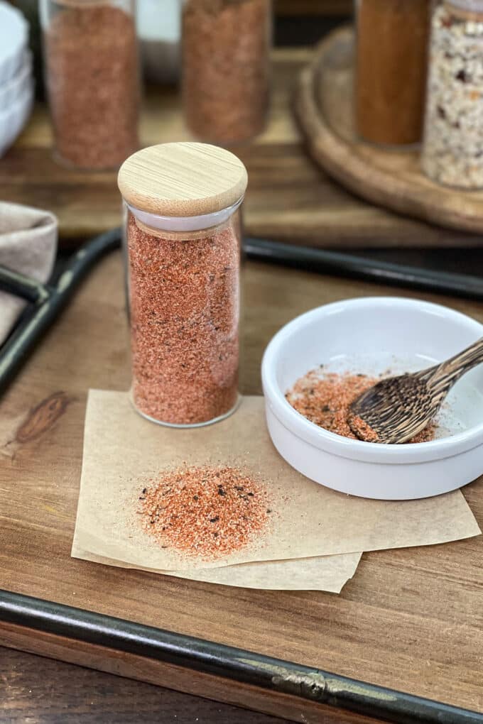 Cajun seasoning in a glass jar, as well as in a white dish with small wooden spoon.