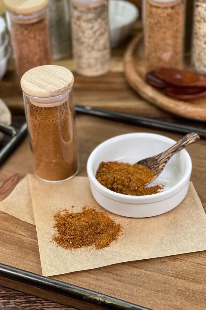 Old Bay seafood seasoning in a glass jar, as well as in a white dish with small wooden spoon.