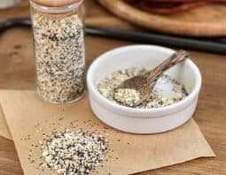Everything Bagel seasoning in glass jar, in dish with spoon, and spilled on parchment paper.