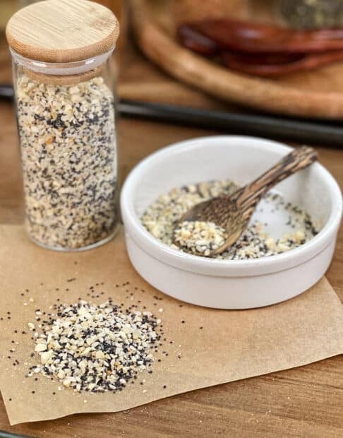 Everything Bagel seasoning in glass jar, in dish with spoon, and spilled on parchment paper.