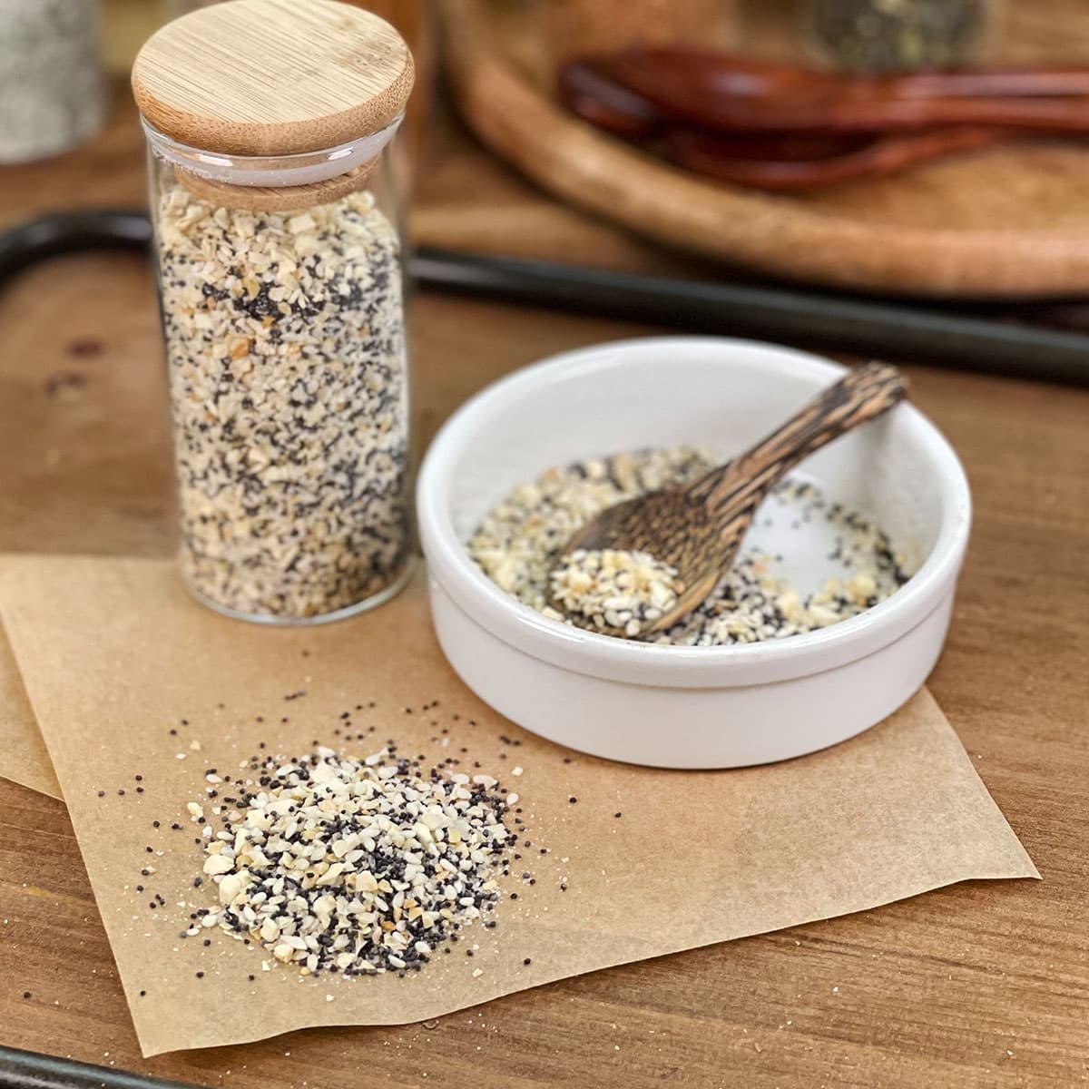 Everything Bagel seasoning in glass jar, in dish with spoon, and spilled on parchment paper.