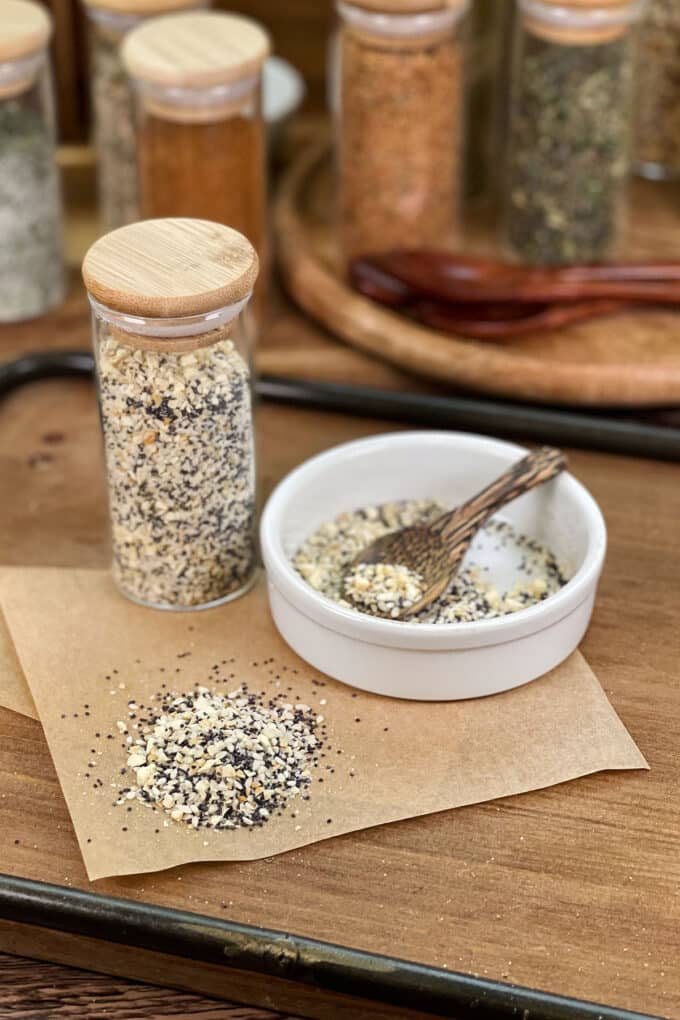 Everything Bagel seasoning in glass jar, in dish with spoon, and spilled on parchment paper.