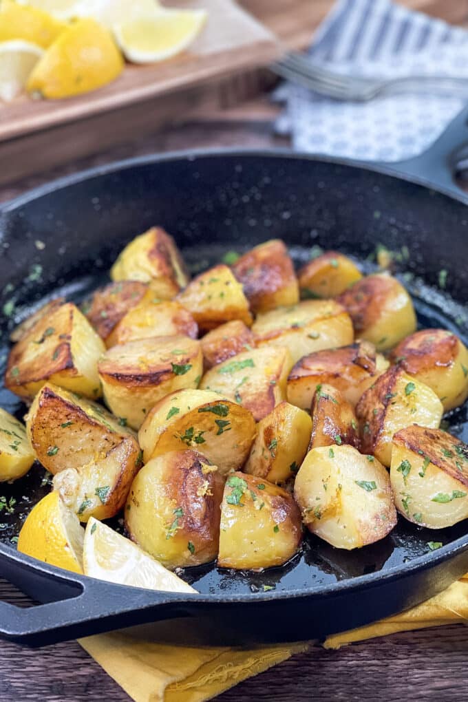 Browned quartered potatoes with lemon and herbs in a cast iron pan.