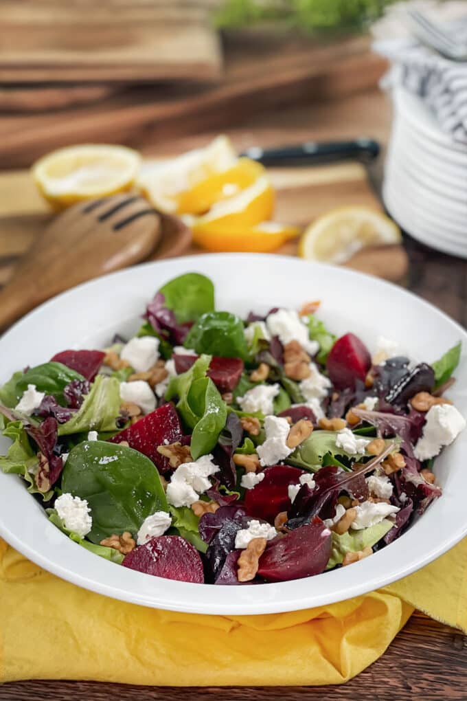 White bowl of salad greens with beets, walnuts, and goat cheese.