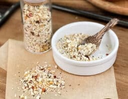 Coarse steakhouse seasoning in glass jar, in dish with spoon, and spilled on parchment paper.
