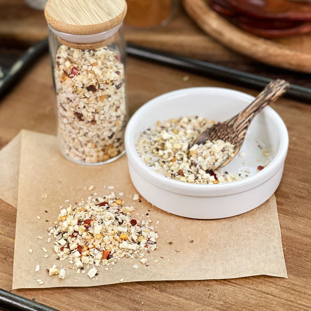 Coarse steakhouse seasoning in glass jar, in dish with spoon, and spilled on parchment paper.