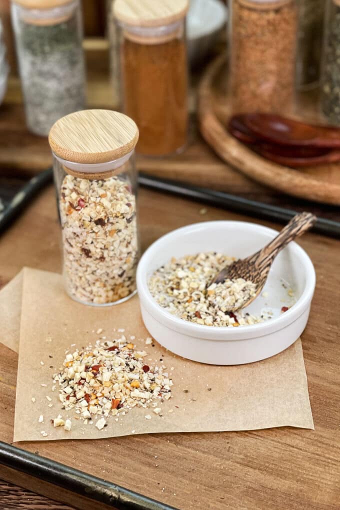 Coarse steakhouse seasoning in glass jar, in dish with spoon, and spilled on parchment paper.