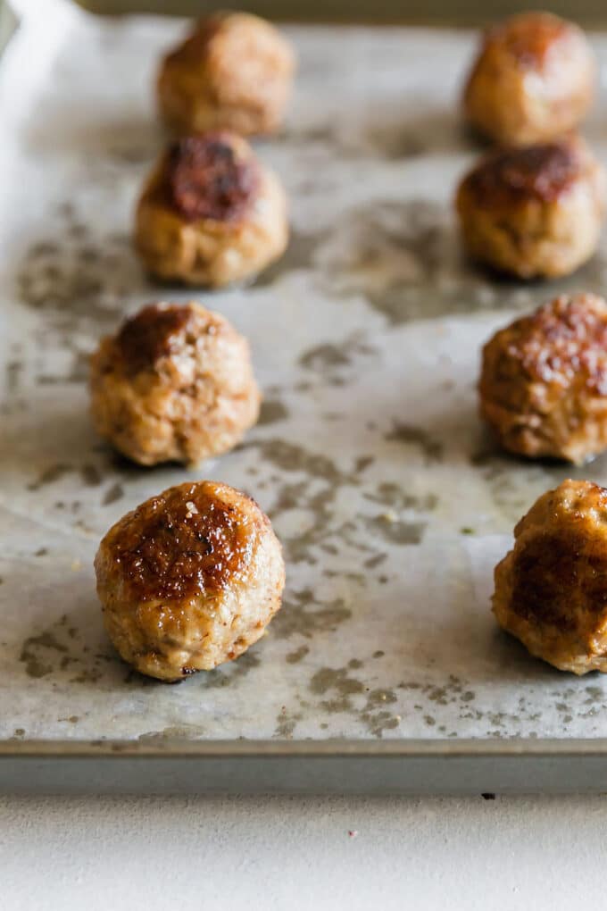 Well-browned meatballs lined up on a pan that has been lined with parchment paper