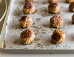 Rows of well-browned meatballs that were baked on a pan that was lined with parchment paper