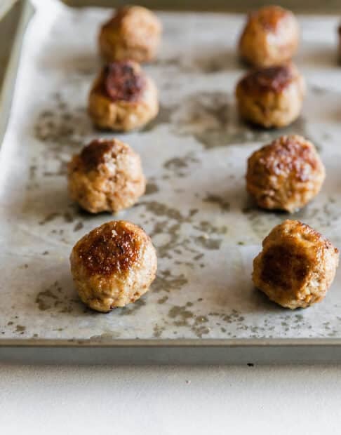 Rows of well-browned meatballs that were baked on a pan that was lined with parchment paper