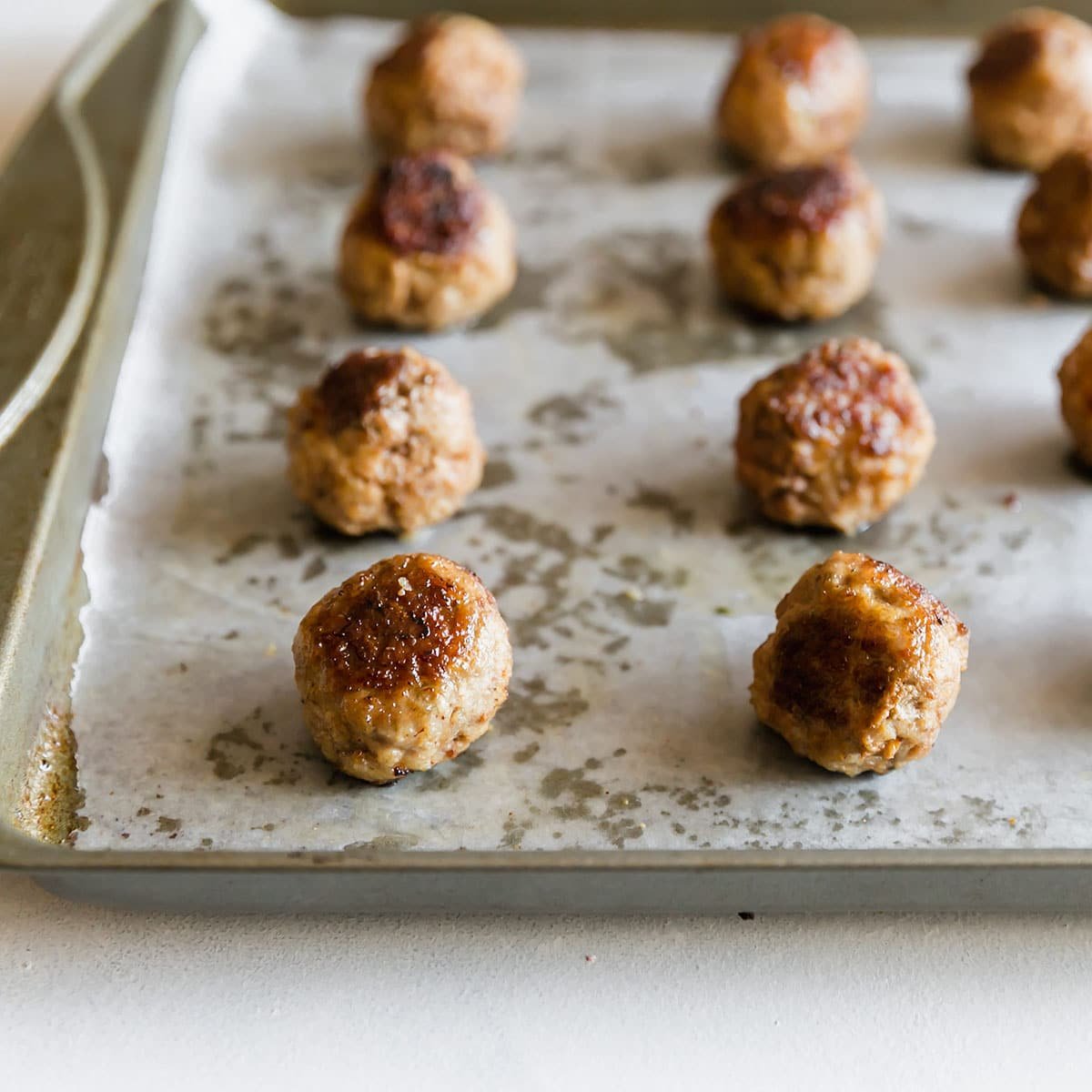 Rows of well-browned meatballs that were baked on a pan that was lined with parchment paper