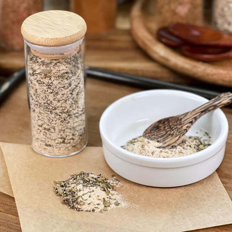 Homemade Creole seasoning in glass jar, in dish with spoon, and spilled on parchment paper.