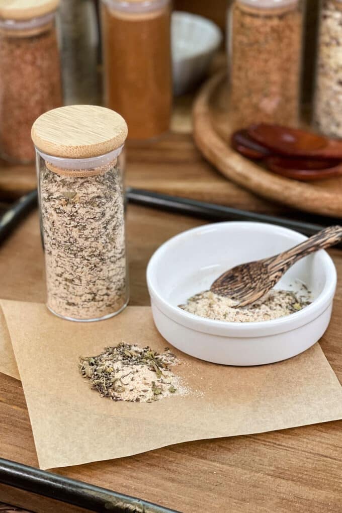 Homemade Creole seasoning in glass jar, in dish with spoon, and spilled on parchment paper.
