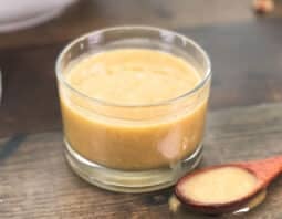 Glass jar and spoon of honey tahini dressing with salad in background.
