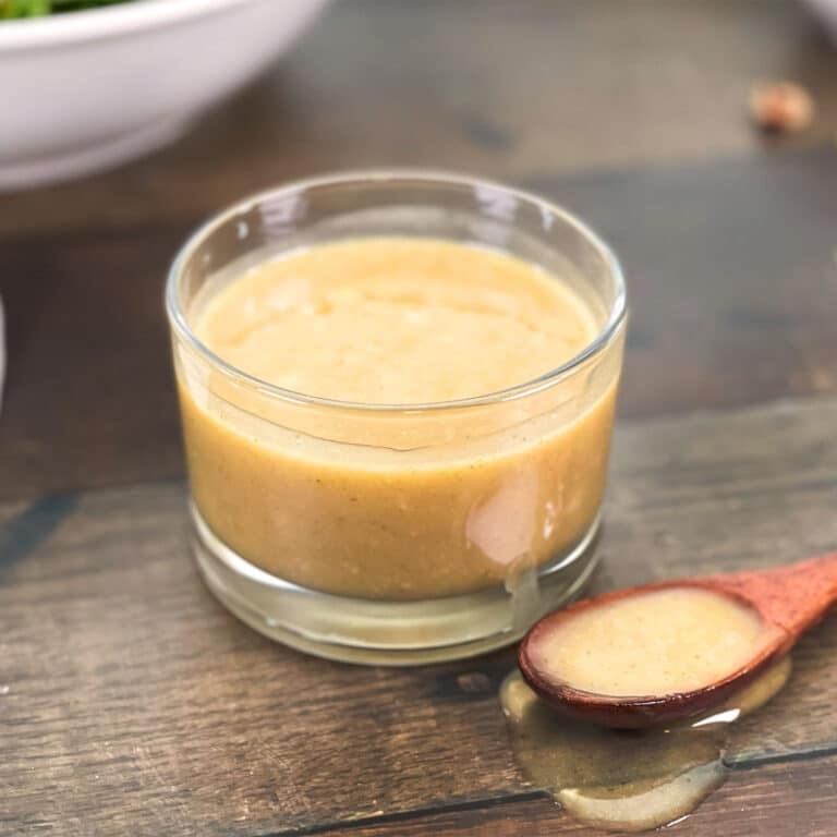 Glass jar and spoon of honey tahini dressing with salad in background.