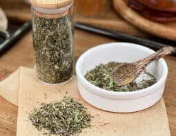 Herbs de Provence with lavender in glass jar, in dish with spoon, and spilled on parchment paper.