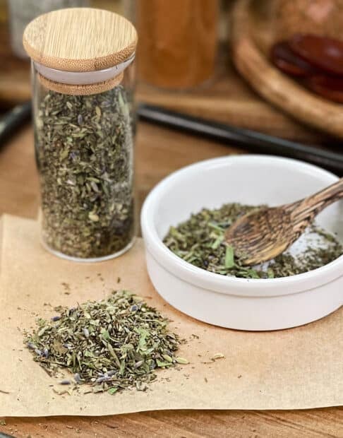 Herbs de Provence with lavender in glass jar, in dish with spoon, and spilled on parchment paper.