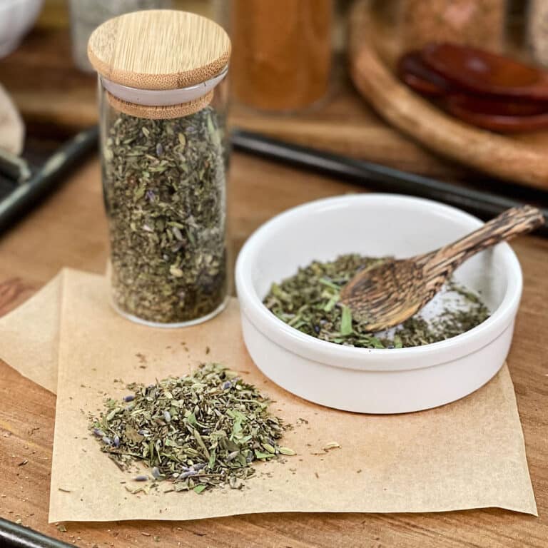 Herbs de Provence with lavender in glass jar, in dish with spoon, and spilled on parchment paper.