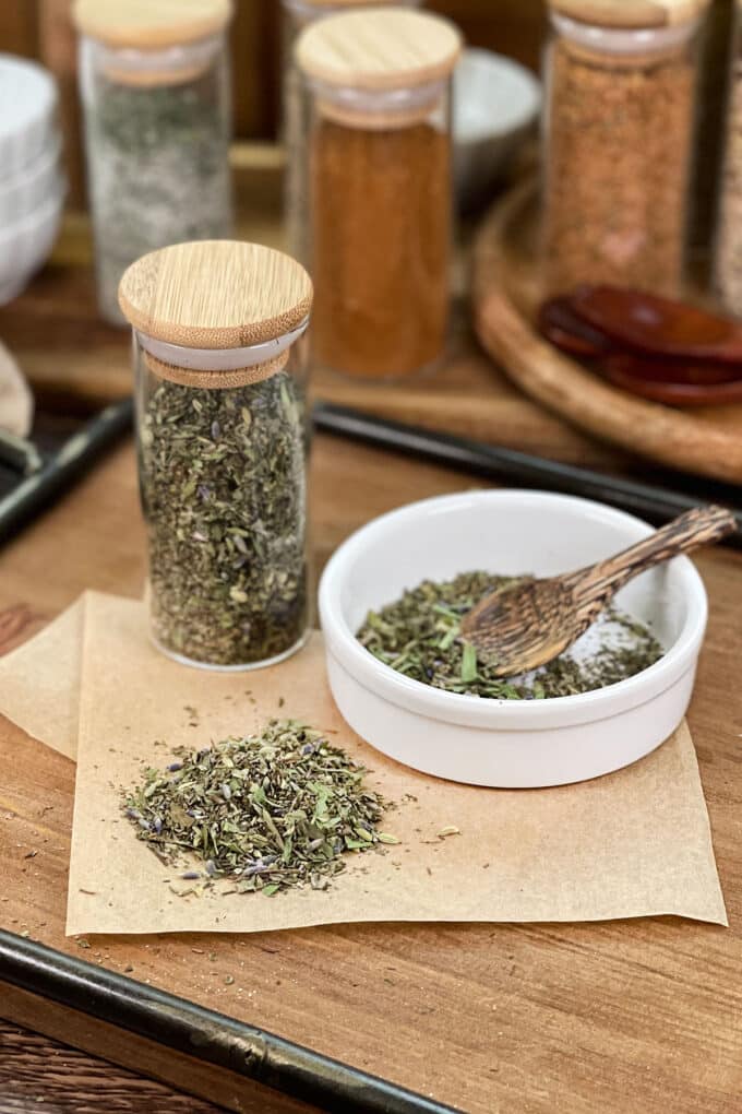 Herbs de Provence with lavender in glass jar, in dish with spoon, and spilled on parchment paper.