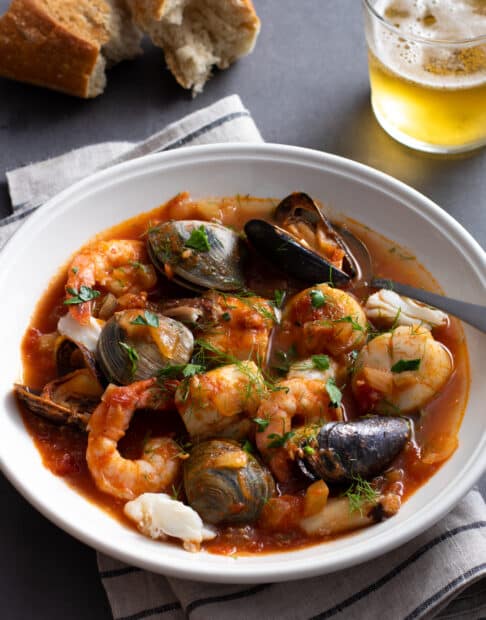 Seafood stew with fish, clams, shrimp, and more in a tomato based broth in a white bowl.
