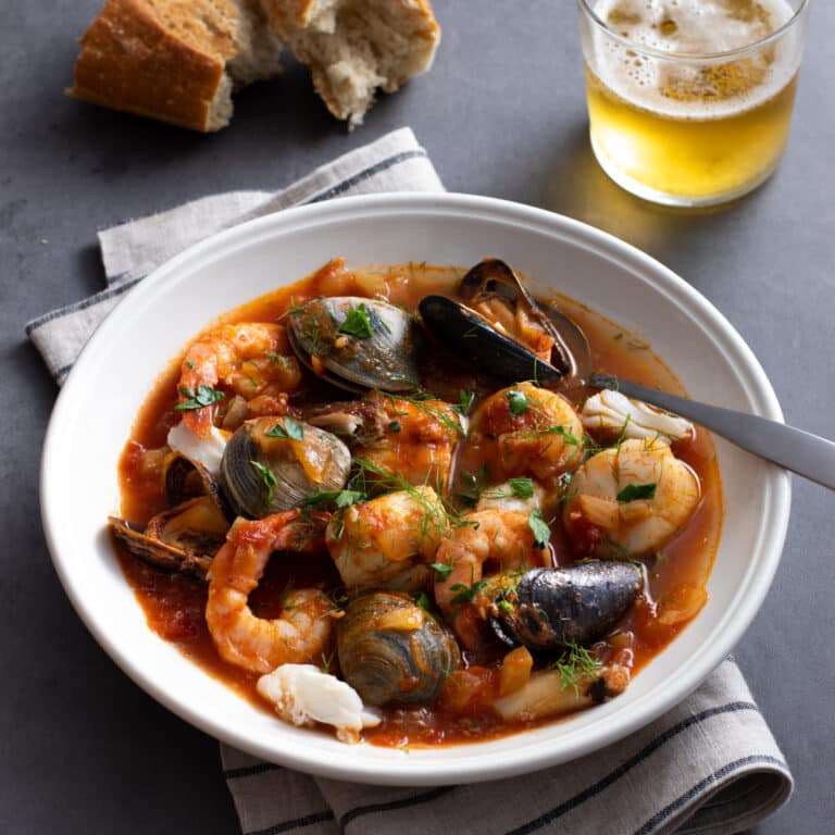 Seafood stew with fish, clams, shrimp, and more in a tomato based broth in a white bowl.