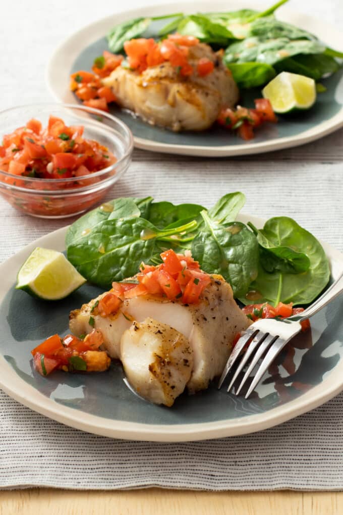 Grilled fish on plate with tomato salsa and salad greens.