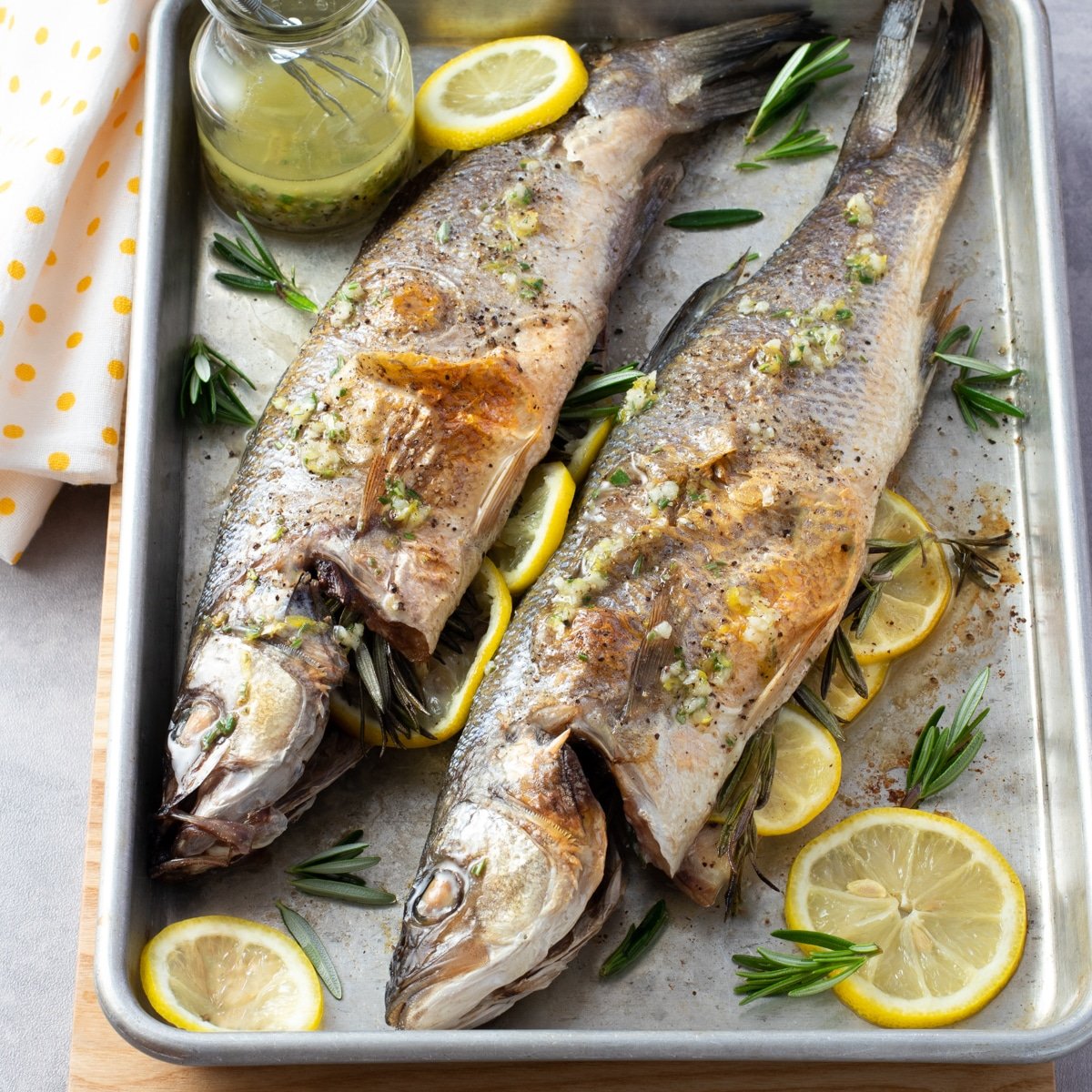 Two whole branzino on a sheet pan with sliced lemon and herbs.