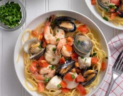 White bowl of pasta with clams, shrimp, mussels, fish, and tomatoes.