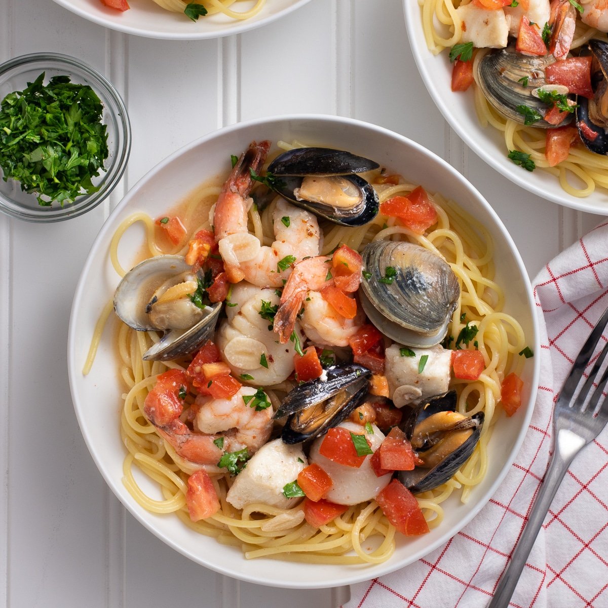 White bowl of pasta with clams, shrimp, mussels, fish, and tomatoes.