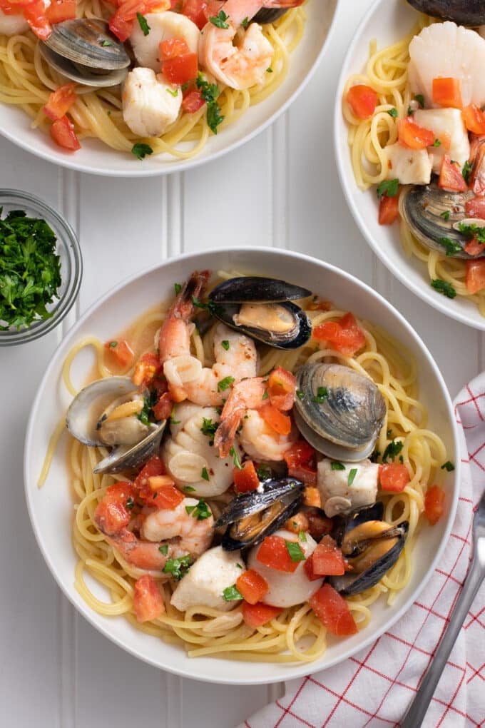 White bowl of pasta with clams, shrimp, mussels, fish, and tomatoes.