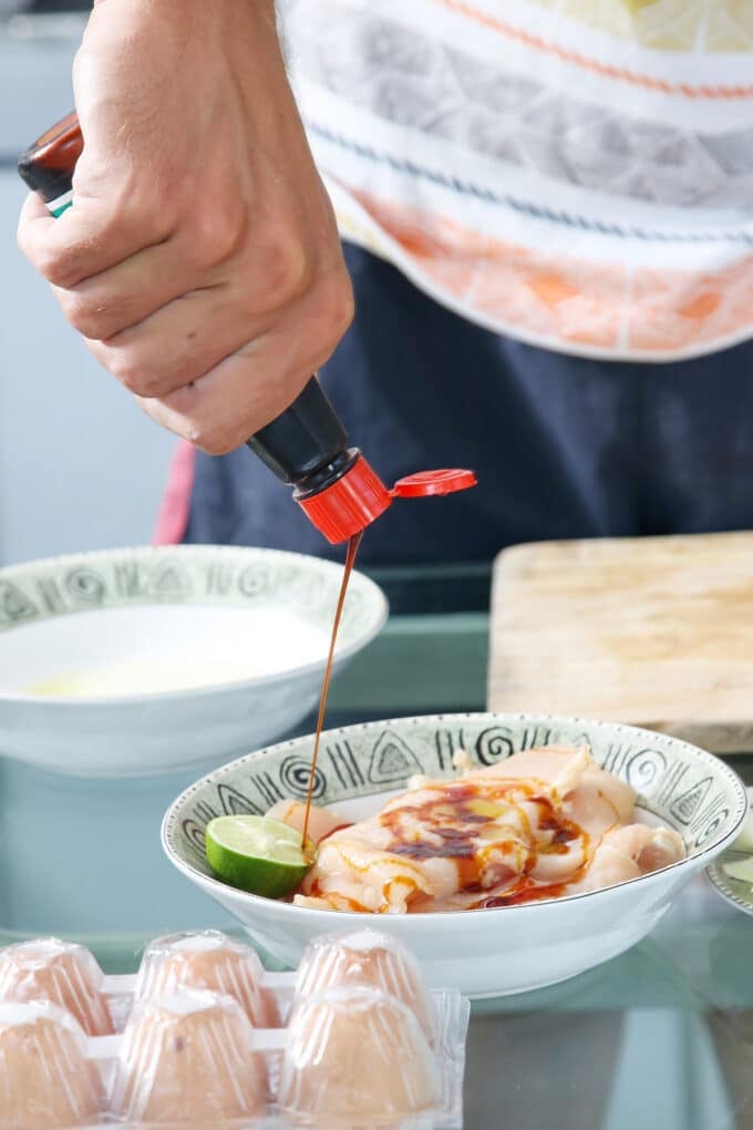 someone pouring soy sauce from a bottle onto raw chicken in a bowl.