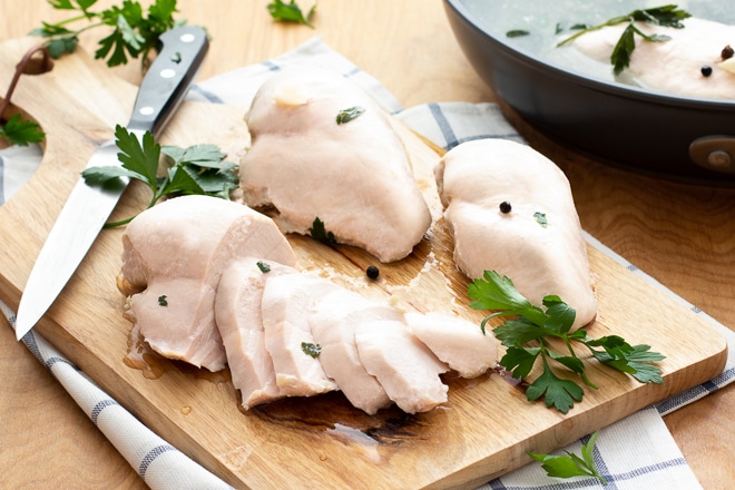Poached and sliced chicken breasts on a wooden board.