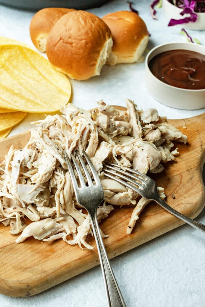 Shredded chicken on a wooden board with two forks.
