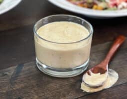 Glass container of lemon hummus dressing and wooden spoon.