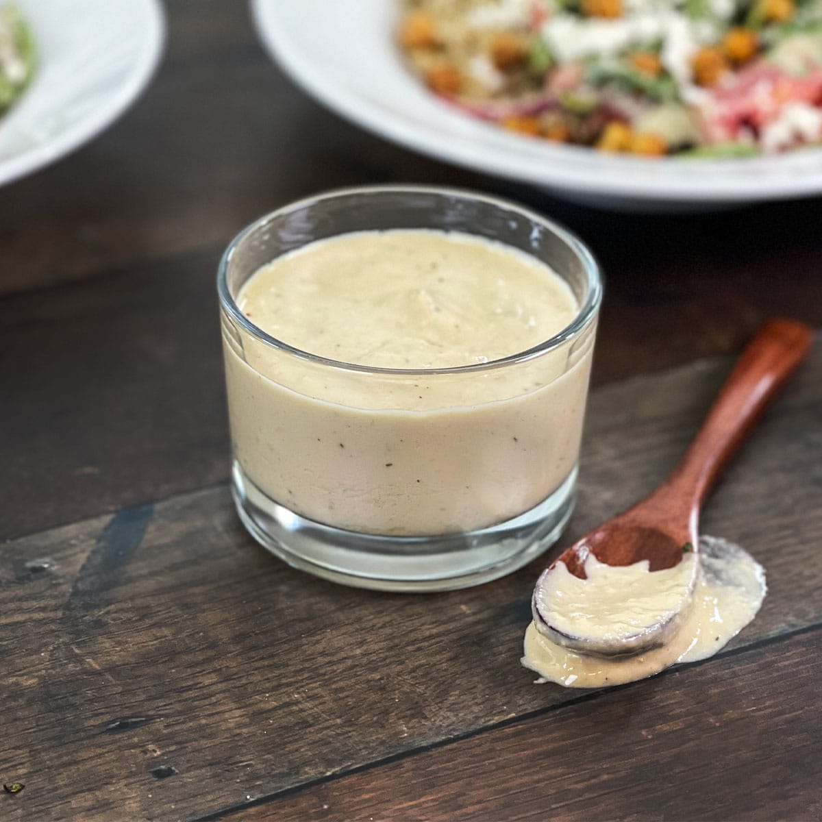 Glass container of lemon hummus dressing and wooden spoon.