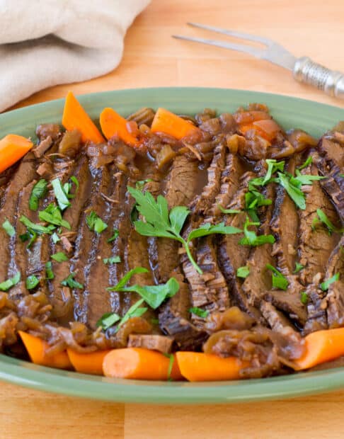 Beef brisket with carrots on a blue-green platter.