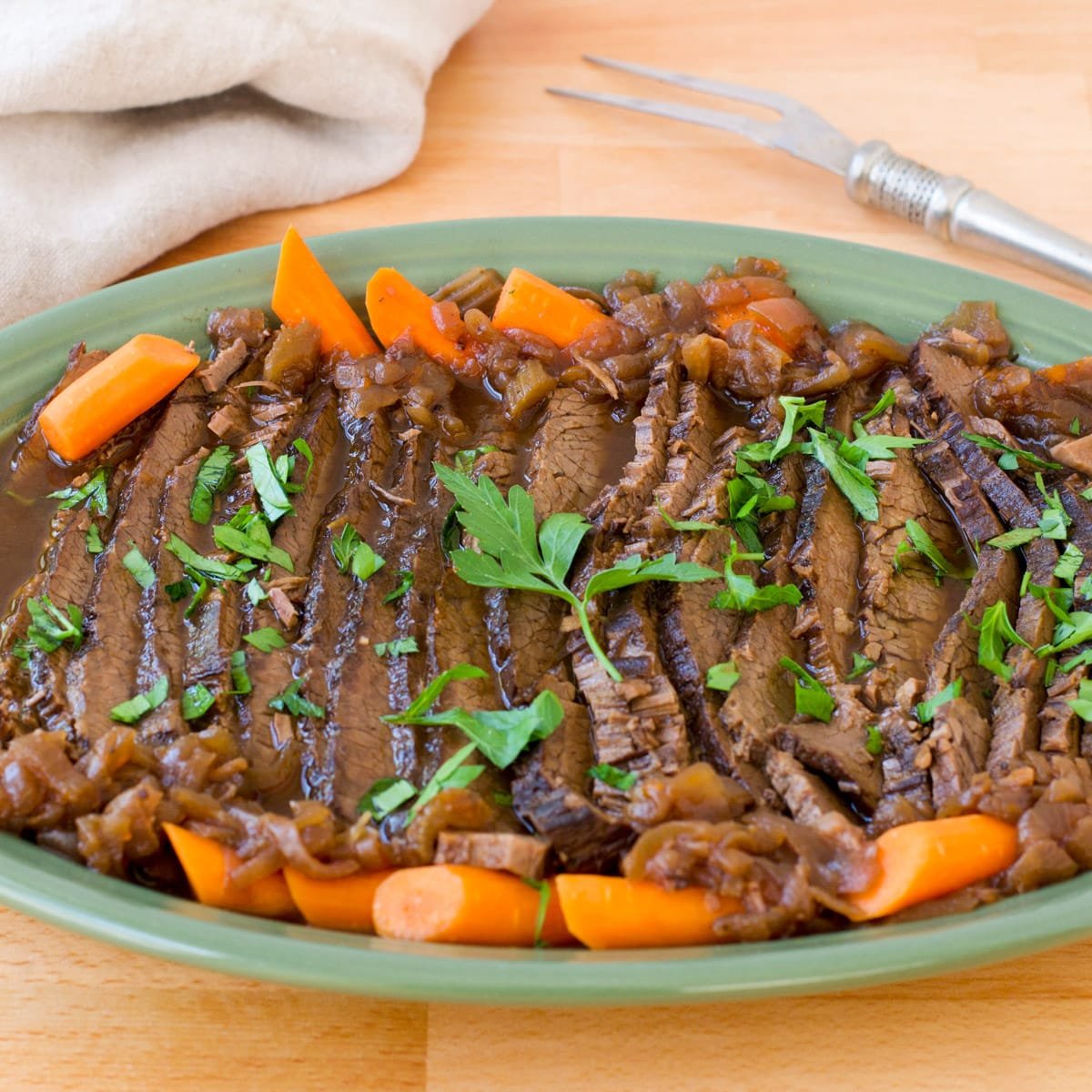Beef brisket with carrots on a blue-green platter.