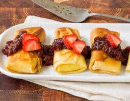 Cheese blintzes topped with jam and fresh strawberry slices.