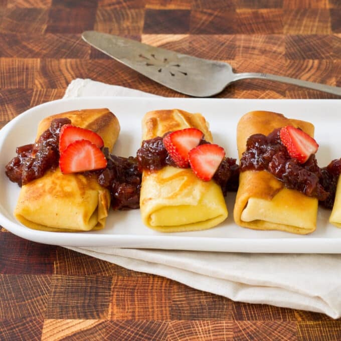 Cheese blintzes topped with jam and fresh strawberry slices.