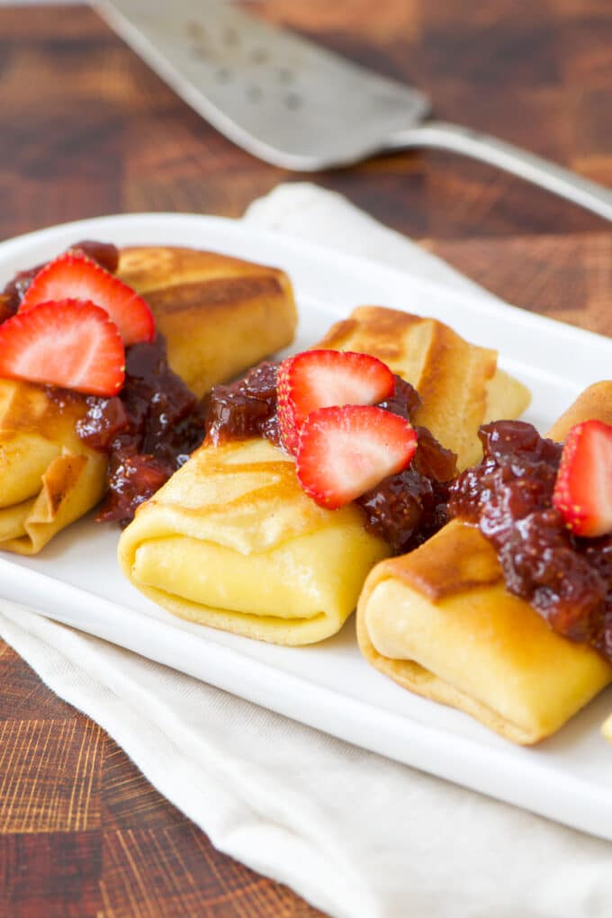 Cheese blintzes topped with jam and fresh strawberry slices.