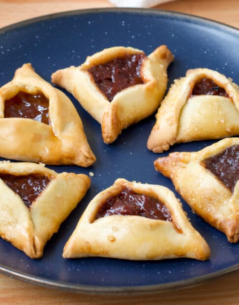 Hamantaschen, jam filled triangular cookies, on a blue plate.