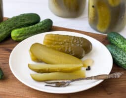 Kosher dill pickles on a white plate and in glass jars.