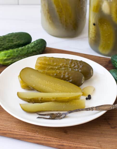 Kosher dill pickles on a white plate and in glass jars.