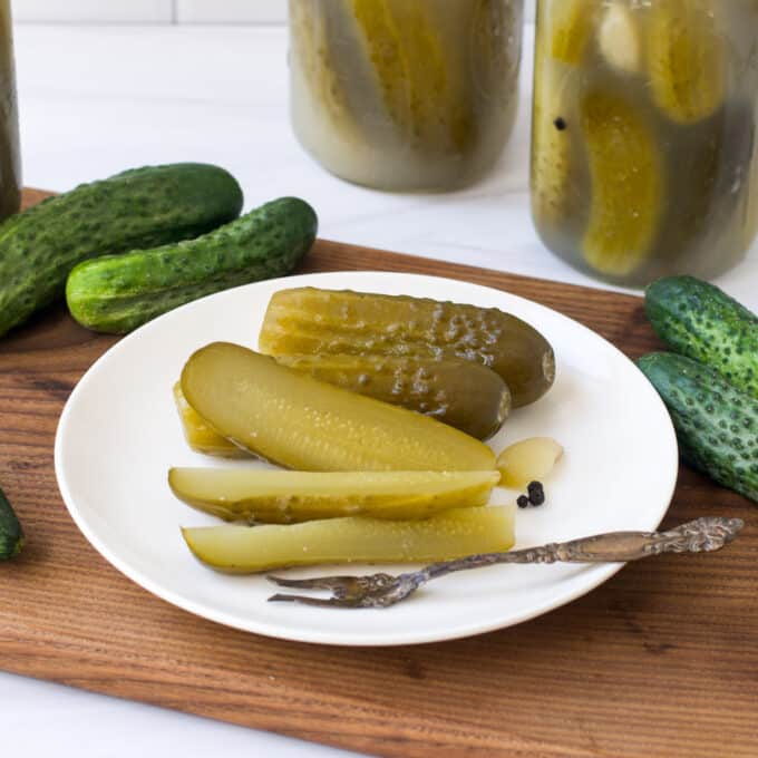 Kosher dill pickles on a white plate and in glass jars.