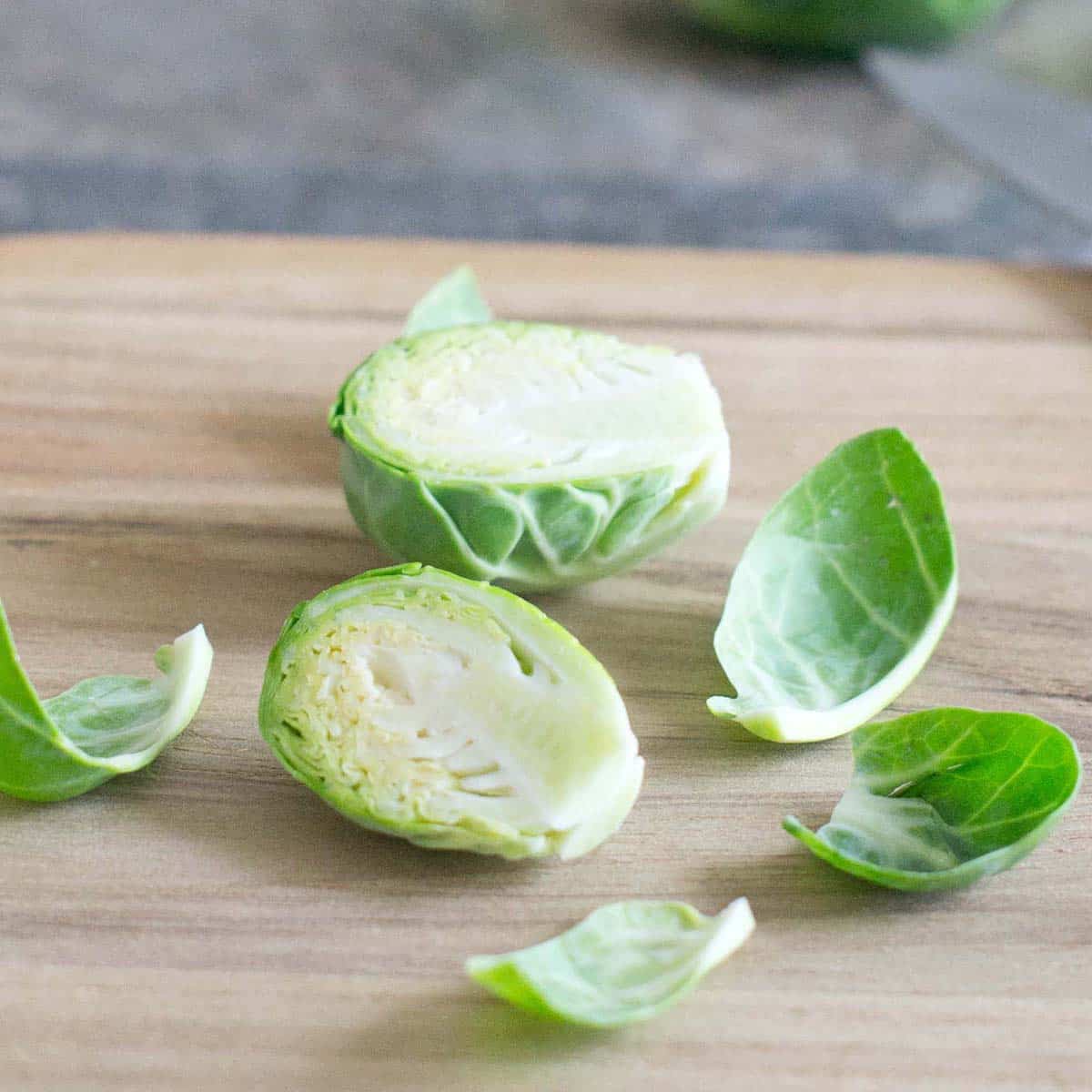 a halved brussels sprout on a cutting board with some loos leaves around it