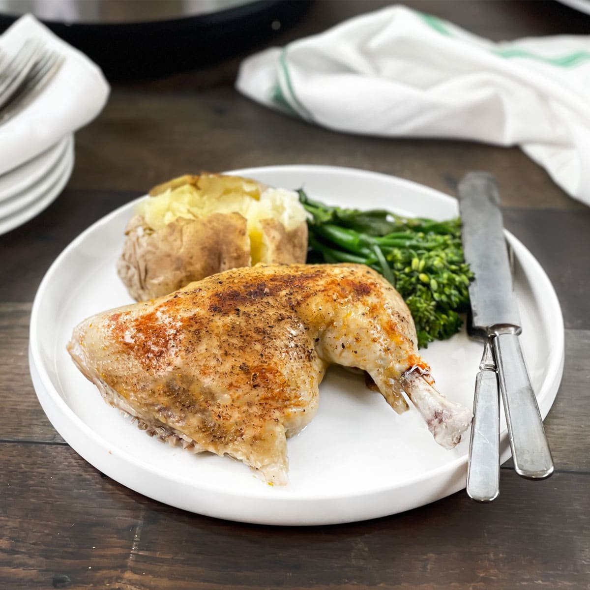 Chicken leg quarter on a white plate with potato and broccolini.