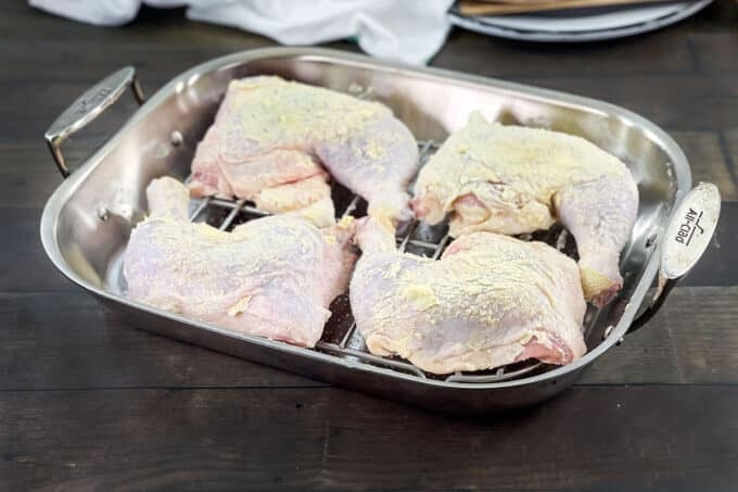 Raw seasoned chicken leg quarters on rack in roasting pan.