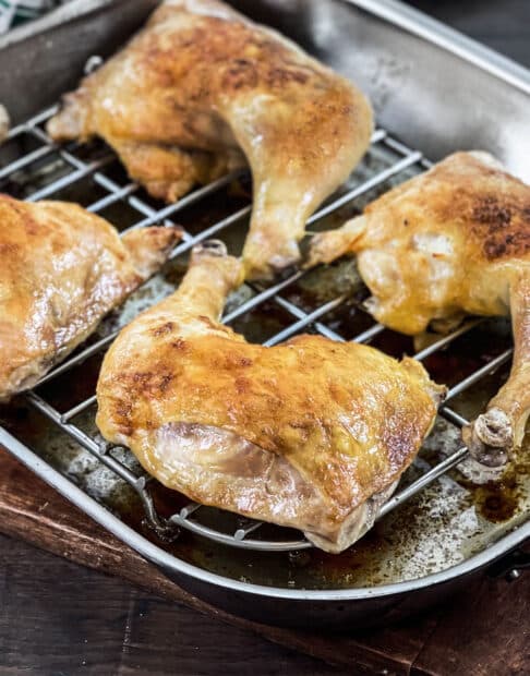 Baked chicken leg quarters on rack in roasting pan.
