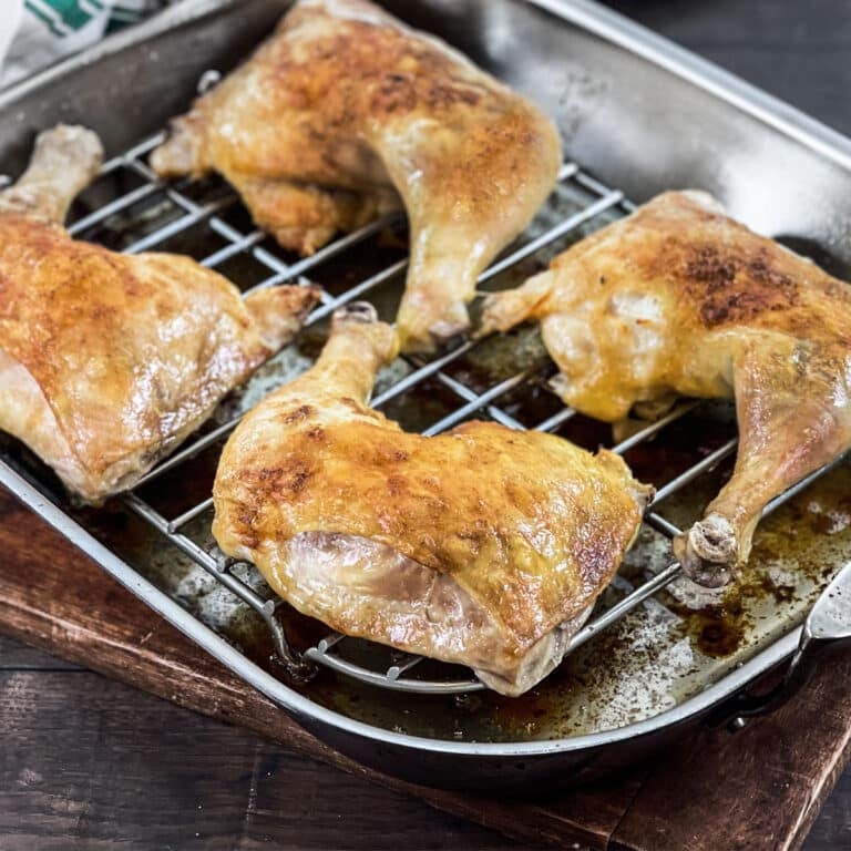 Baked chicken leg quarters on rack in roasting pan.